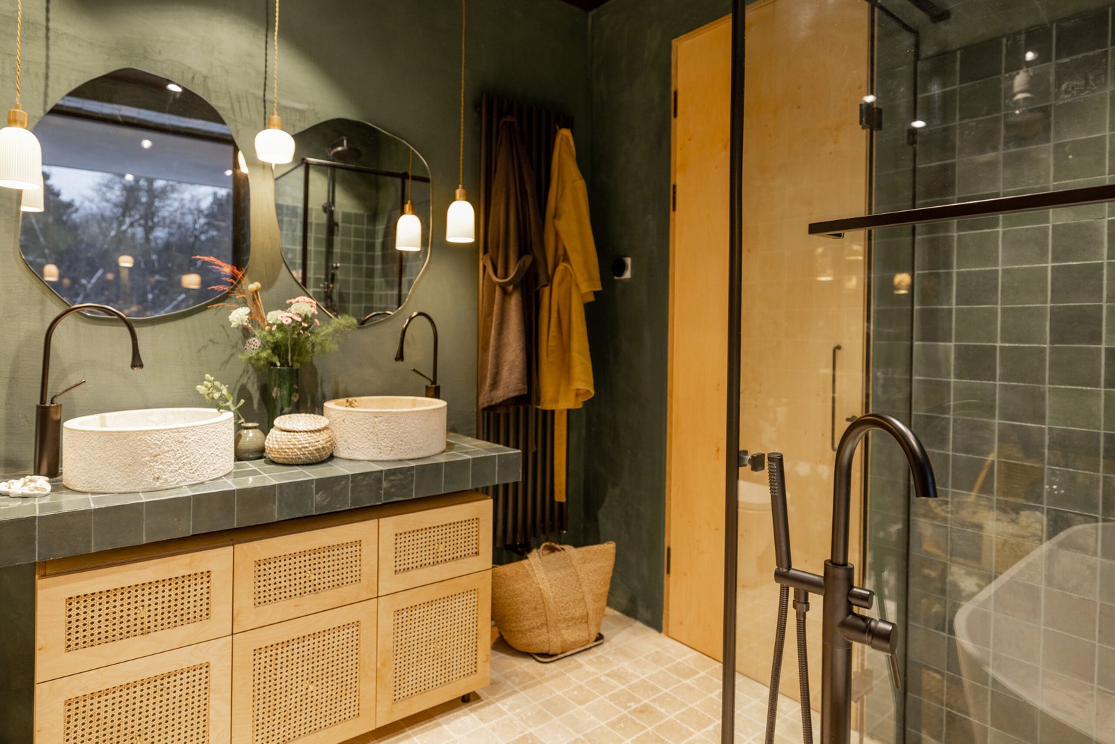 Bathroom interior with stone wash basins, modern faucets, irregularly shaped mirrors and wooden rattan commode in green and beige tones in natural boho style