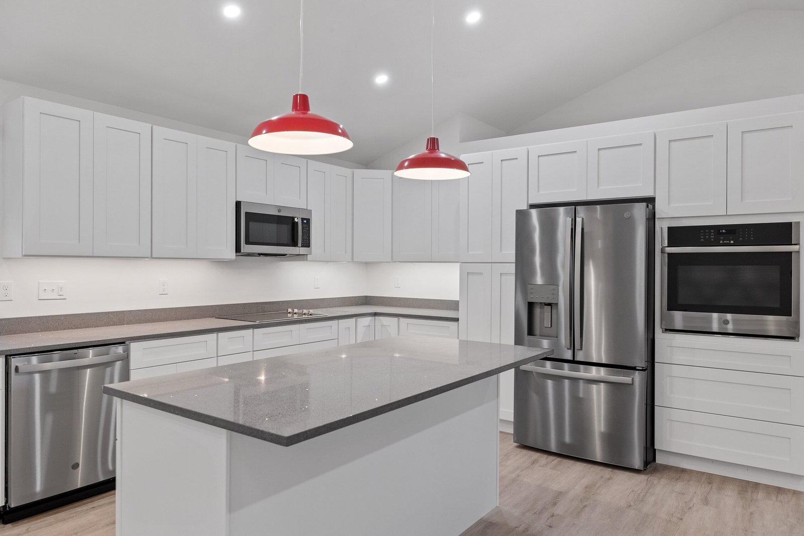 The interior of a kitchen with white cabinets, red hanging lamps, a parquet floor and electrical appliances