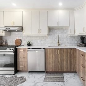 A bright modern kitchen with white upper cabinets, wood-grain lower cabinets, gold handles, and a marble tile floor. The space features stainless steel appliances, a white quartz countertop, and a glossy subway tile backsplash.